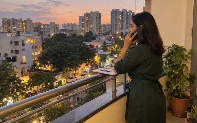 A woman on a phone call on a flat balcony in Bangalore in the evening