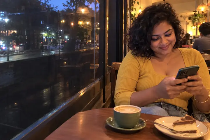 A girl in a small cafe smiling at a message on her phone